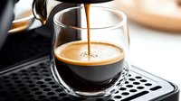 Fresh espresso pouring from coffee machine into glass cup on metal drip tray, creating rich crema layer with golden brown color and smooth texture.