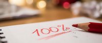 Red pencil marking 100 percent score on white paper notebook with warm bokeh lights creating academic achievement and success concept for education.