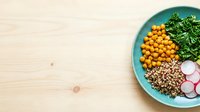 Overhead view of turquoise bowl with chickpeas, lentils, fresh greens, and radish slices on light wooden surface. Healthy eating and meal prep concept.