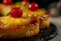 Gourmet dessert slices topped with glossy caramel glaze, maraschino cherries, and candied fruit garnish on dark plate for bakery, pastry, and food photography.