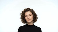 Young professional woman with curly brown hair wearing black top against white background, isolated portrait for business and corporate design projects.