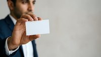 Middle-aged man with olive skin tone wearing formal business attire holding blank white card for networking, branding, or corporate communication purposes.