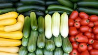 Fresh colorful summer vegetables arranged in rows including yellow squash, dark and light green zucchini, and red cherry tomatoes creating vibrant pattern.