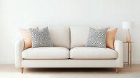 Modern cream colored sofa with polka dot pattern pillows and peach accent cushions against white wall, wooden floor lamp creates minimalist living room setting.
