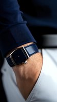 Elegant navy leather watch with minimalist black dial on male wrist, wearing dark blue suit sleeve and white shirt, capturing modern luxury lifestyle.
