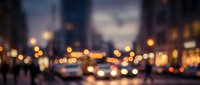Urban street at dusk with blurred city lights, traffic, and buildings creating a bokeh effect. Suitable for backgrounds and design projects.
