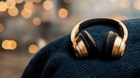 Gold wireless headphones on blue knitted fabric with warm bokeh lights in background creating cozy atmosphere for music listening experience.