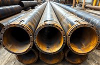 Large industrial metal pipes with flanged ends stacked in warehouse storage area, showing raw steel construction materials for pipeline infrastructure.