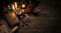 Mystical fortune telling setup with tarot cards, candles, crystal ball and ancient books on rustic wooden table for divination and spiritual guidance.