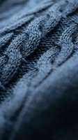 Close-up macro shot of blue knitted wool fabric texture showing detailed cable knit pattern and fiber structure for fashion and textile design projects.
