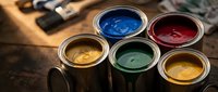 Open paint cans with colorful paints in blue, red, yellow and green colors with paintbrushes on wooden surface for home renovation and creative projects.