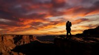Silhouette of male hiker standing on rocky mountain peak at dramatic sunset with golden orange sky and clouds, adventure and exploration concept for travel and outdoor lifestyle.