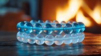 Blue and clear crystal beaded bracelets on dark wooden surface with warm fireplace glow in background, spiritual wellness and meditation accessories.