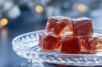 Translucent red jelly cubes on crystal plate with soft bokeh background create elegant dessert composition. Glowing gelatin squares catch light dramatically.