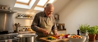 Senior Caucasian man cooking fresh vegetables in modern kitchen with skylights, preparing healthy meal at home, retirement lifestyle cooking hobby.