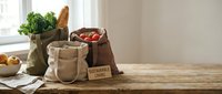 Eco-friendly reusable shopping bags filled with fresh organic groceries on rustic wooden kitchen counter promoting sustainable zero waste lifestyle.