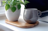 Gray ceramic coffee mug on wooden tray with green plant and laptop creating modern workspace atmosphere for home office productivity and relaxation.