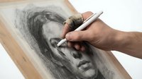 Artist hand drawing realistic portrait with charcoal pencil on paper, creative process of sketching human face with professional art supplies and techniques.