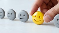 Hand holding yellow smiley face among gray neutral expressions on white surface, representing positive attitude, happiness, optimism and mental wellness for business and lifestyle use.