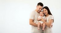 Happy young Caucasian family with baby posing together in matching beige outfits against white background for portrait photography and family memories.