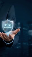 Businessman hand presenting uptime guarantee shield symbol for reliable service and system availability in corporate technology environment.