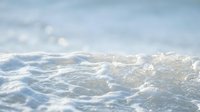 Sunlit ocean waves with white foam crests rolling across blue-green water under bright sky, suitable for travel, nature, and coastal design projects.