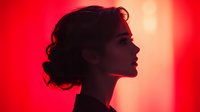 Young Asian woman silhouette profile against vibrant red background with dramatic lighting and elegant updo hairstyle creating mysterious atmospheric mood for fashion and beauty concepts.