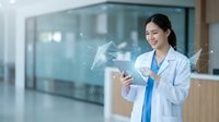 Asian female doctor in white coat using digital tablet with holographic interface in modern hospital corridor for healthcare technology and medical innovation.