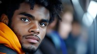 Young African American man in orange hoodie looking thoughtfully aside against blurred urban background, expressing contemplation and determination in modern setting.