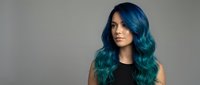Young woman with vibrant blue-green ombre hair and wavy hairstyle against neutral background for beauty and fashion concepts.