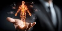 Digital hologram of human anatomy with glowing skeleton and organ systems displayed above businessman's hand against dark background.