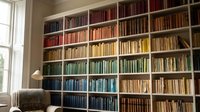 Elegant home library with color-coordinated books arranged by rainbow spectrum on white built-in shelves, cozy reading chair by window for interior design.