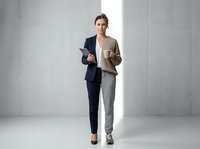 Professional businesswoman in modern suit walking confidently with tablet in contemporary office space for corporate presentations and leadership concepts.