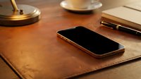 Modern smartphone on leather desk pad with coffee cup and pen creating elegant workspace atmosphere for business productivity and communication.