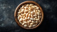 Fresh white butter beans in wooden bowl on dark stone background, top view. Raw legumes for healthy vegetarian cooking and protein-rich diet.