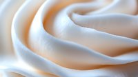 Smooth swirls of creamy white meringue or whipped cream texture forming elegant curves and waves in macro photography, soft focus background creates dreamy effect.