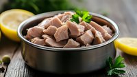 Raw chicken hearts in black ceramic bowl with fresh parsley and lemon slices on rustic wooden background, close up view of fresh meat preparation.