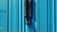 Legs and feet of person wearing formal against bright turquoise blue corrugated metal wall, casting dramatic shadow in sunlight.