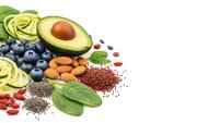 Fresh superfood ingredients including avocado, blueberries, almonds, chia seeds, quinoa and spinach arranged on white background for healthy nutrition.