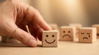 Hand placing a wooden cube with a smiley face among blocks showing various emotions, symbolizing positivity and mental wellness choice.