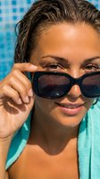 Young woman with tan skin and dark wet hair adjusting black sunglasses at swimming pool, summer vacation and leisure lifestyle concept for travel and wellness marketing.