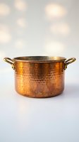 Hammered copper pot with brass handles on white surface with warm bokeh lights background for cooking and kitchen decor.