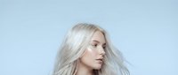 Young blonde woman with flowing platinum hair in profile against clean white background for beauty and fashion projects.