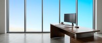 Modern executive office workspace with dark wooden desk, computer monitor, and floor-to-ceiling windows overlooking clear blue sky, suitable for corporate, business, and professional design projects.