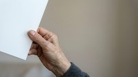 Senior adult hand with visible age spots and wrinkles holding blank white paper against neutral background, suitable for healthcare, aging, communication, or document-related concepts.