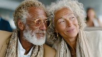 Happy senior African American man with curly gray beard and elderly Caucasian woman with white curly hair smiling together in warm embrace showing love and joy.