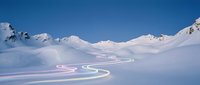 Winding mountain road with light trails through snowy alpine landscape at dusk, aerial view of winter terrain with curves for travel and transportation concepts.