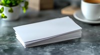 Stack of blank white business cards or paper mockup on gray marble table with coffee cup and plant in background, ready for branding presentation.