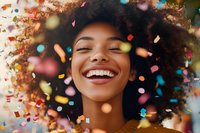 Young African American woman with natural curly hair laughing joyfully while colorful confetti falls around her face, expressing genuine happiness and celebration.