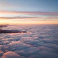 Breathtaking aerial view above fluffy white clouds at sunrise with soft pink and orange sky colors creating dreamy atmospheric landscape for travel content.